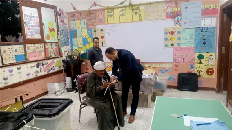 رئيس لجنة انتخابية يساعد مسنًا للإدلاء بصوته في سوهاج